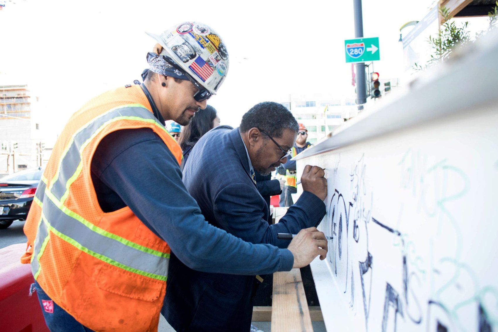 Talmadge signs name on wall alongside construction worker.