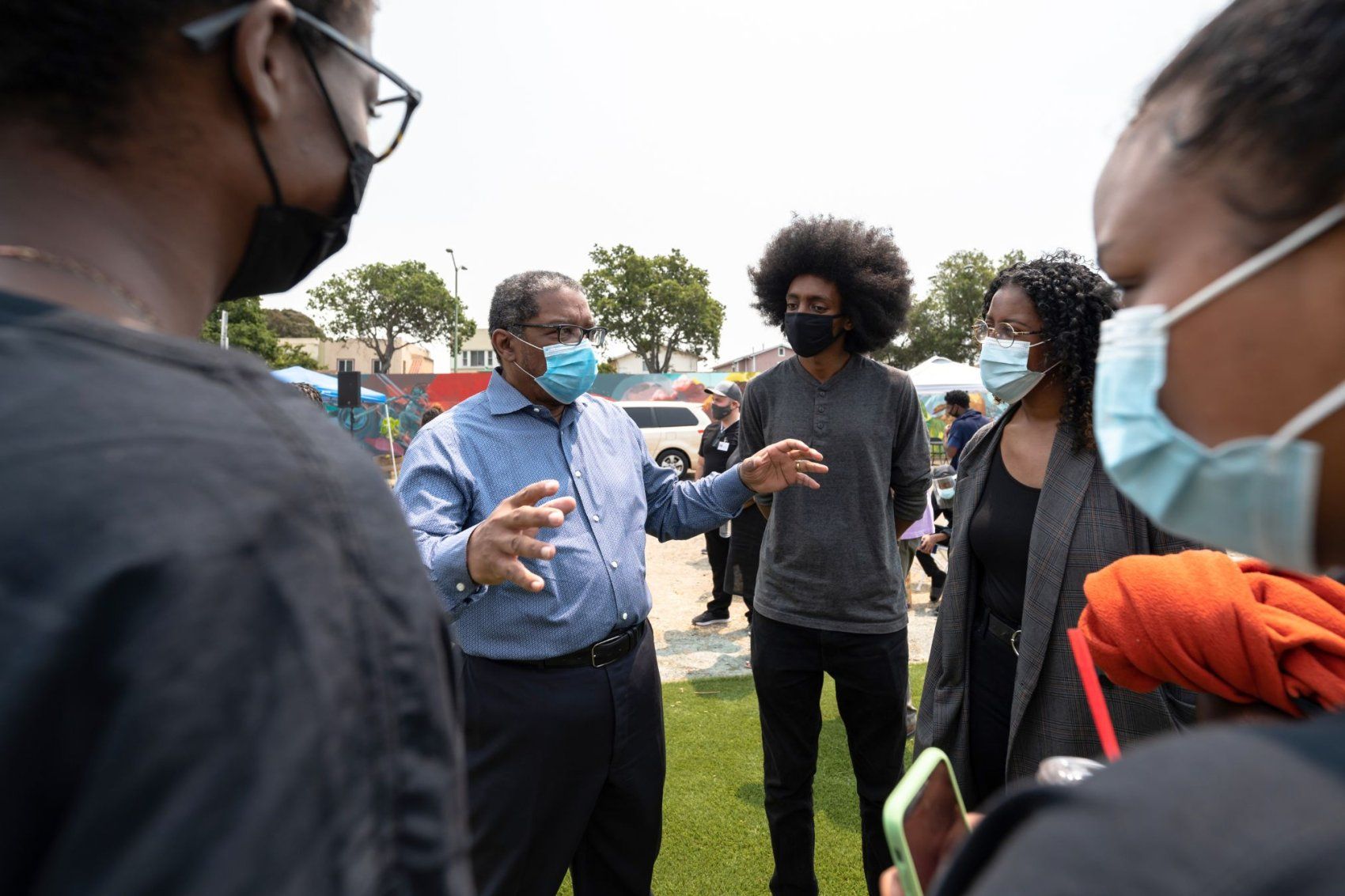 Talmadge in an outdoor community huddle wears protective mask.