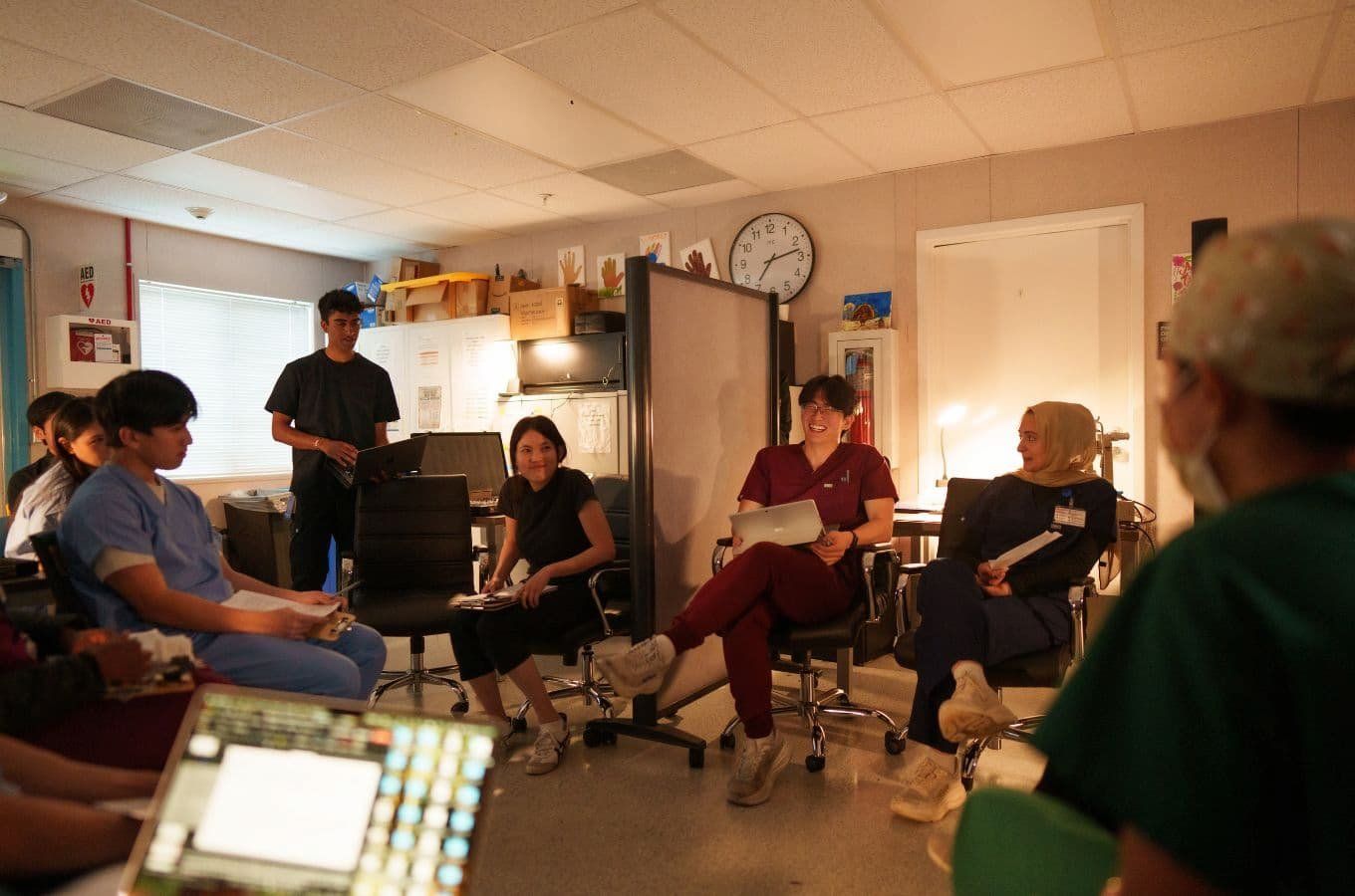 A group of medical students and medical professionals sit together and have a lively discussion in a room bathed in evening light.