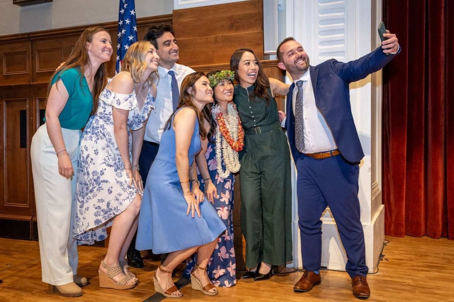 A group of smiling UCSF Fresno surgery graduates in academic regalia pose together for a selfie on stage during commencement.