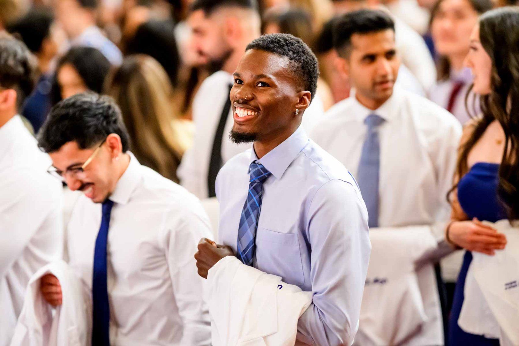 Medical students smile as they hold their white coats during a ceremony.