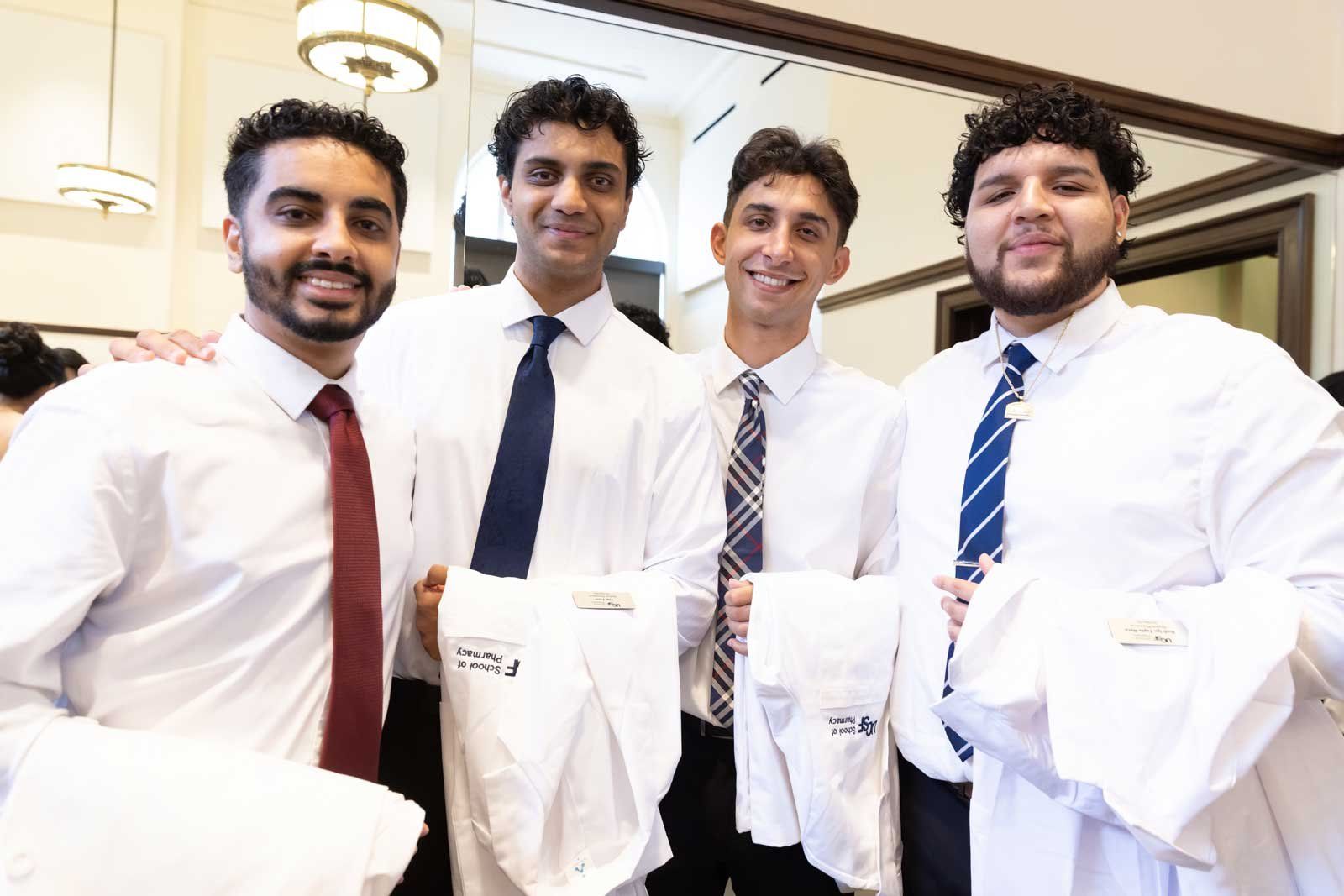 Four UCSF School of Pharmacy students pose together while holding their new white coats.