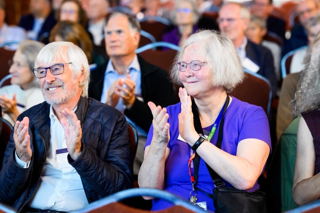 Reg Kelly and Elizabeth Blackburn clap as they sit in an audience.