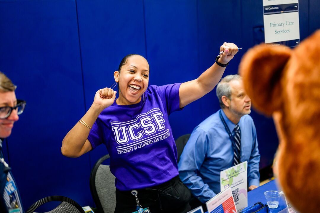 Psychologist Nocole Reinosa poses energetically as she greets students while wearing a purple U C S F shirt.