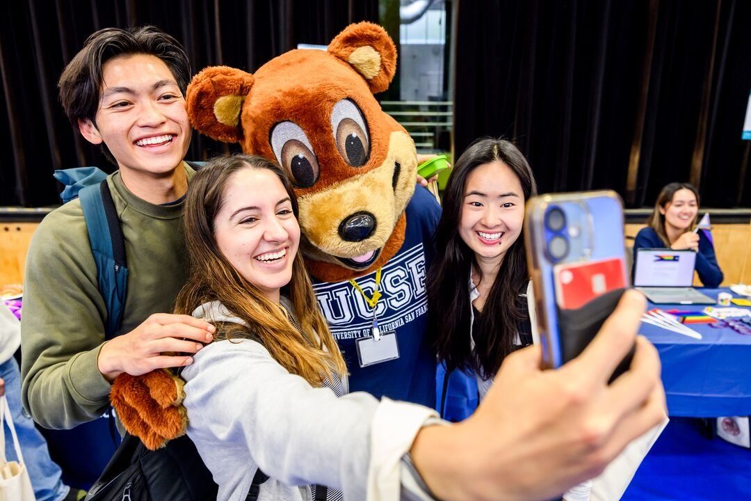 Three medical students take a selfie with U C S F's bear mascot.
