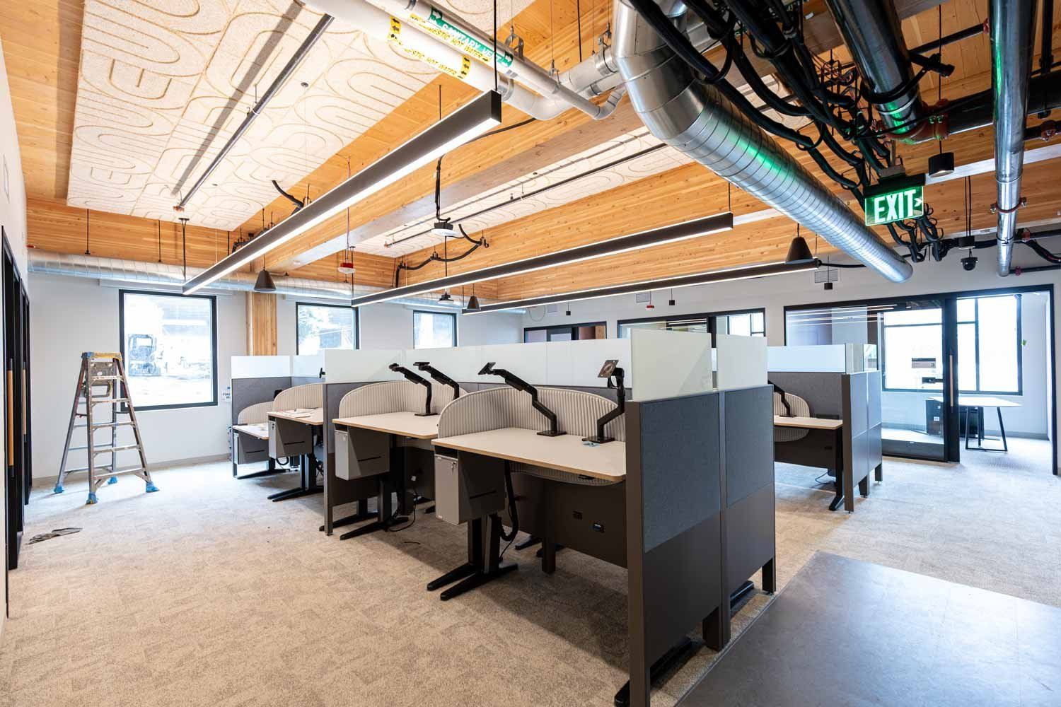 Open office workspace with rows of desks, exposed wood ceilings, hanging lights and visible ductwork inside Temescal Hall.