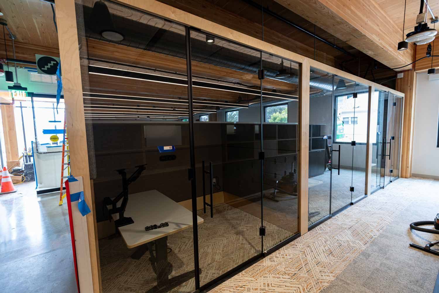 Glass-walled meeting rooms inside Temescal Hall, with exposed wood beams and ceilings visible throughout the space.