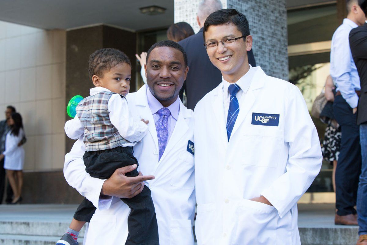 Derrell Washington holds his son while posing for a photo with new dentistry classmate Manabu Manadhar