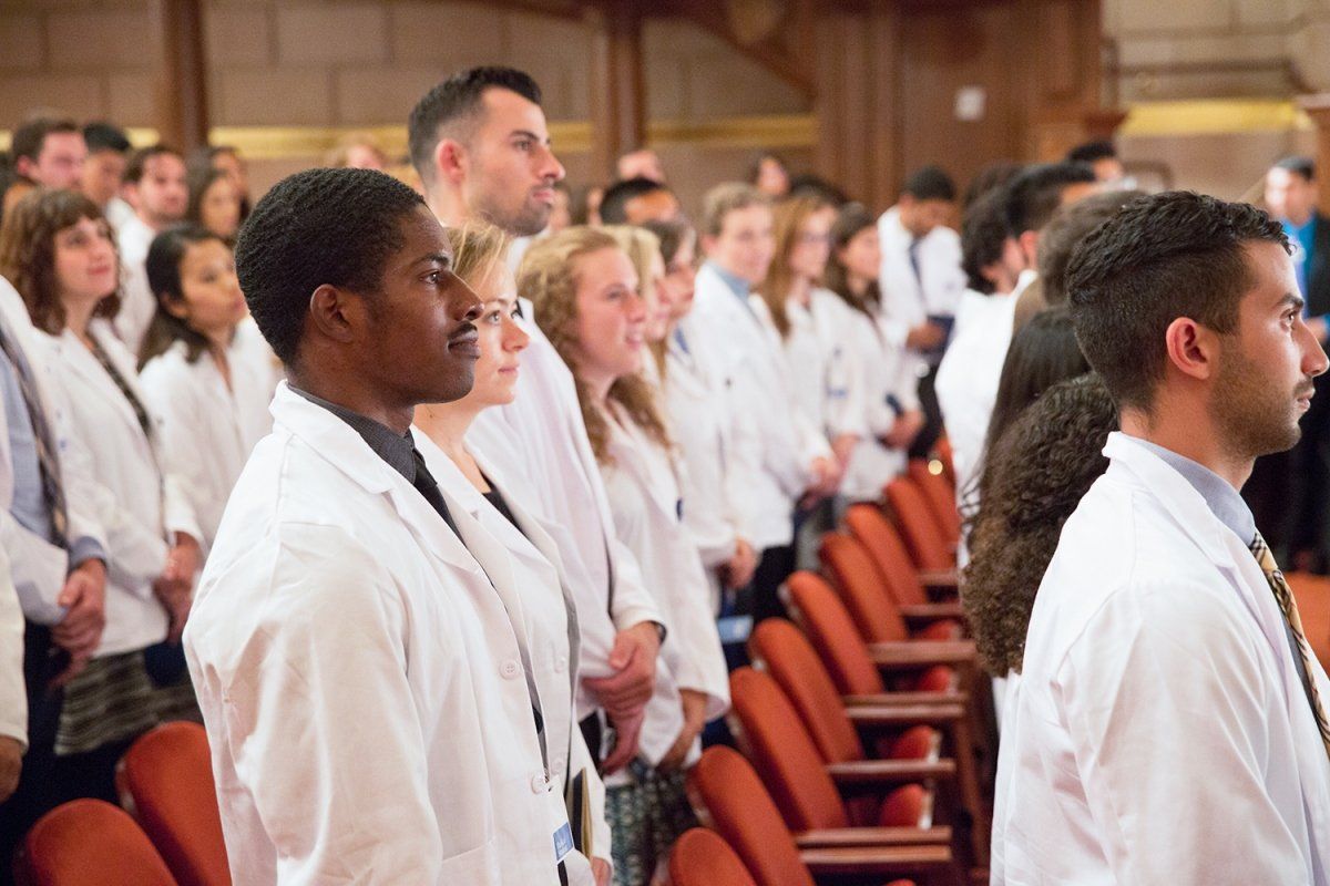 Wearing their new white coats, new School of Medicine students stand during a ceremony