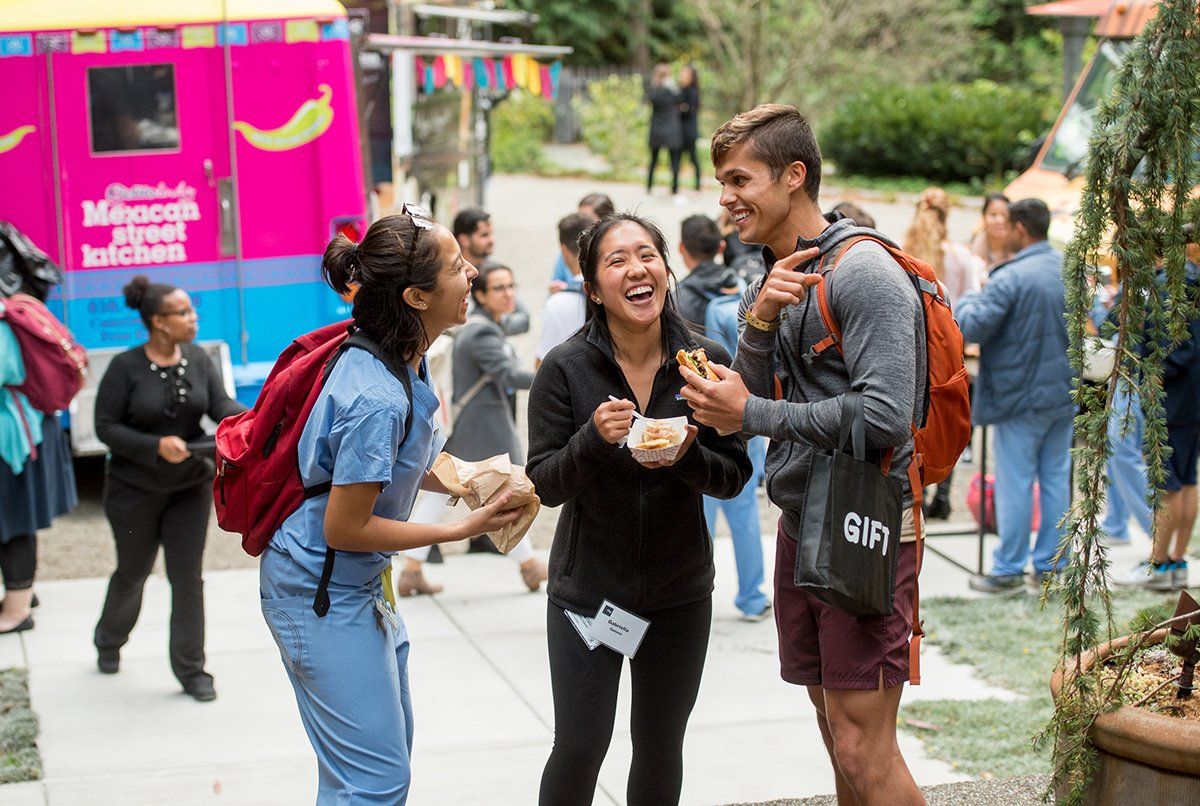 A group of three students enjoy food and laugh during an event at the UCSF Chancellor’s Residence