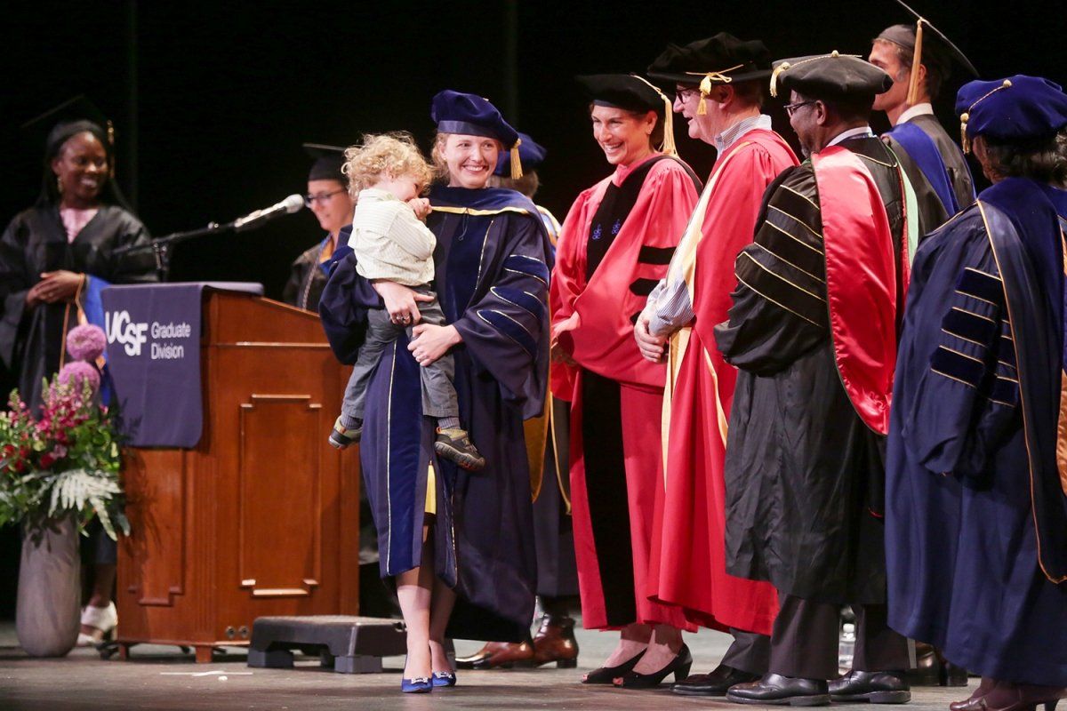 Meg Vigil-Fowler walks across the stage holding her son Rafa during the Graduate Division commencement ceremony