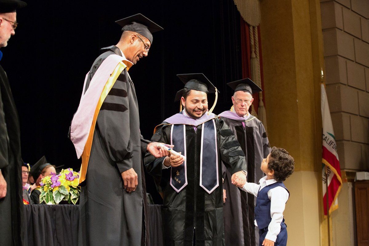 Bishoy Joseph Besada receives his diploma with his son during the School of Dentistry commencement