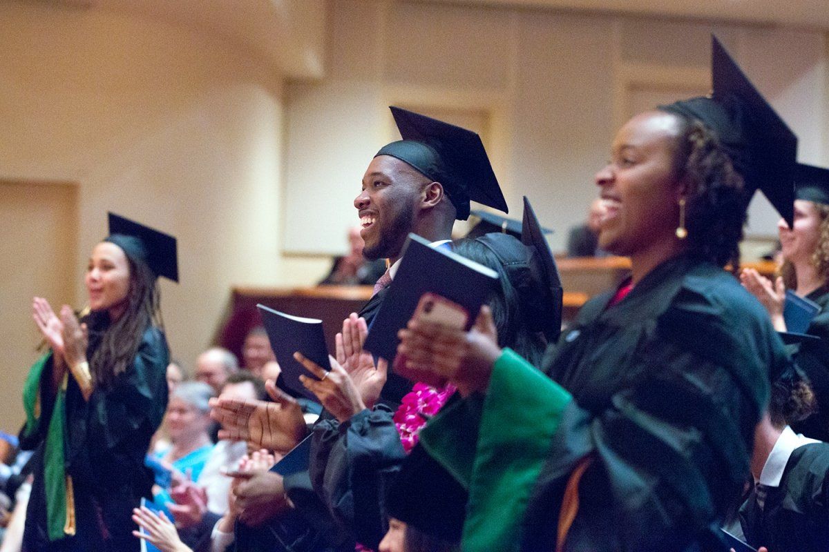 School of Medicine students Kadia Wormley, Cheikh Njie and Sidra Bonner stand and clap during the commencement ceremony