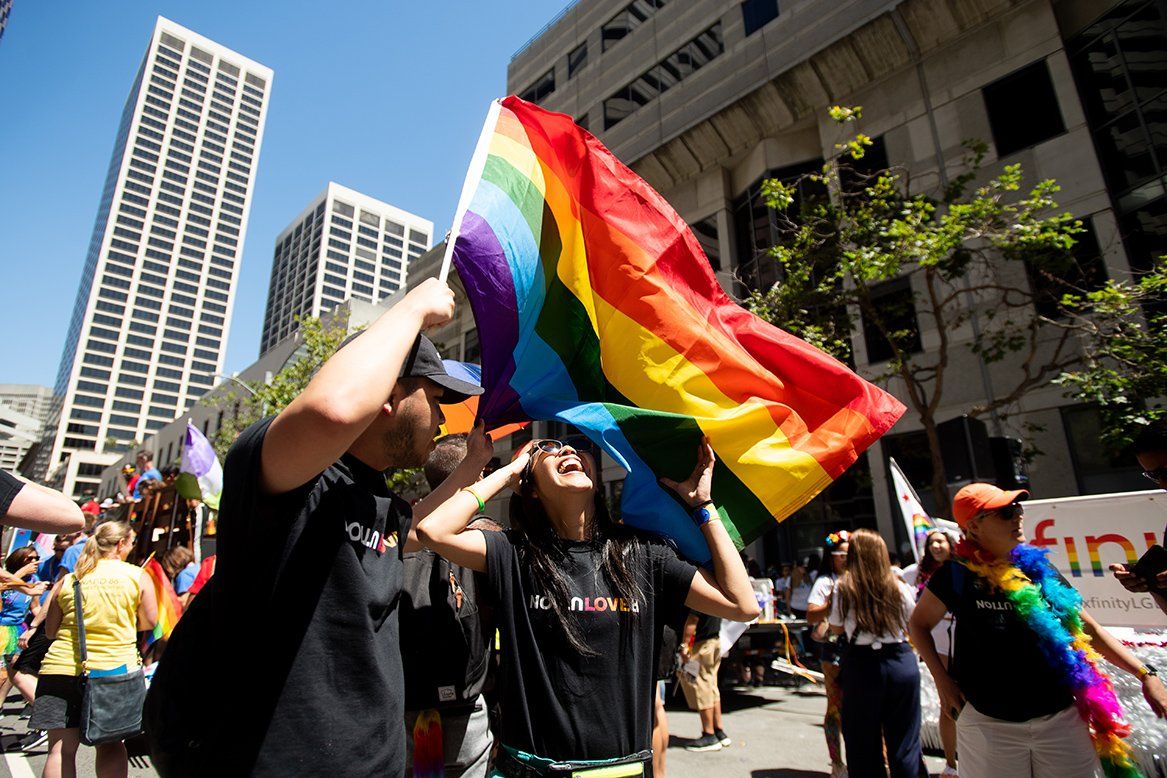 A woman laughs as a man holds rainbow flag above her