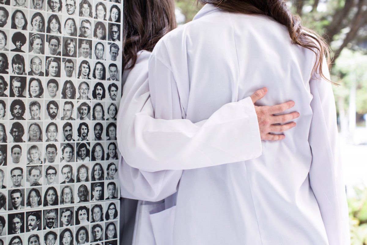 two students wearing white coats stand with their back to the camera