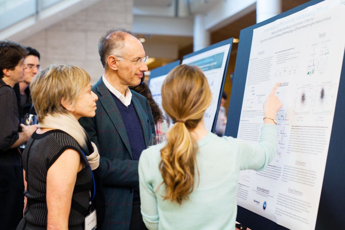 Sir Michael Moritz and Harriet Heyman discuss research with a fourth-year Discovery Fellow Meghan Zubradt (Biomedical Sciences) at the first Discovery Fellows Symposium