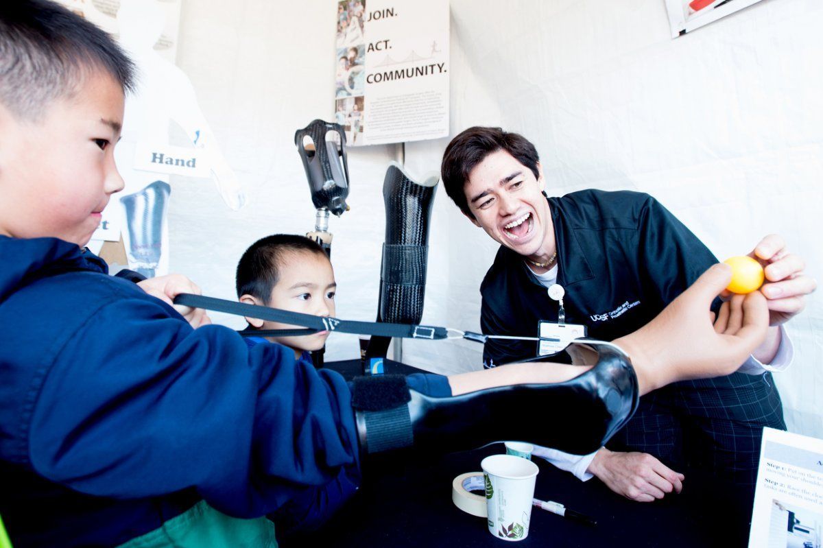 Matthew Chen helps two boys use a prosthetic arm