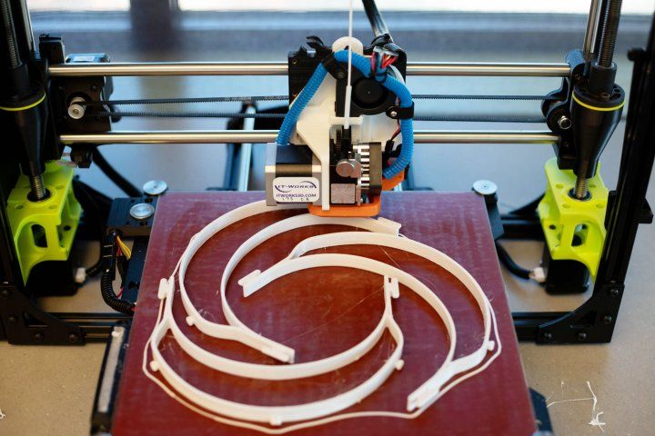 3D printer making three white headbands for face shields