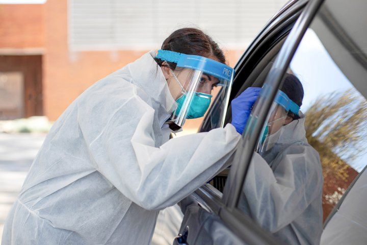 nurse wears an N95 mask and face shield while testing a person for COVID-19