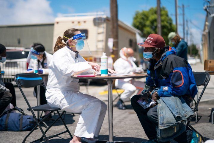Clinician in PPE talks to unhoused man at an outdoor table