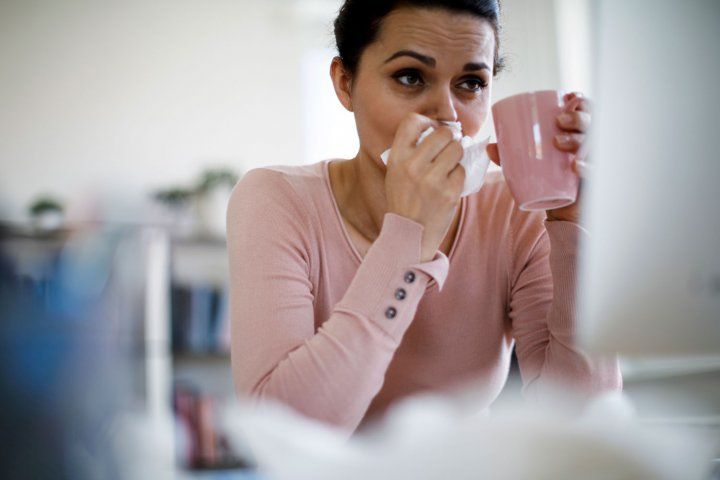 Woman blowing nose and holding mug