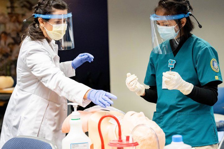 a nursing instructor points at a dummy while a student looks on