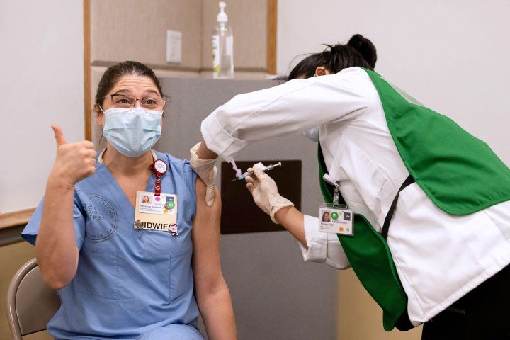 Woman in scrubs give thumbs up while receiving vaccine