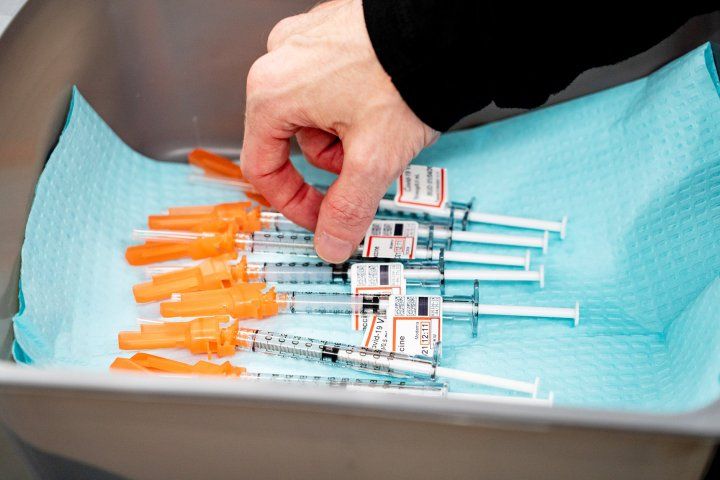 a hand reaches for a COVID-19 vaccine sitting in a tray