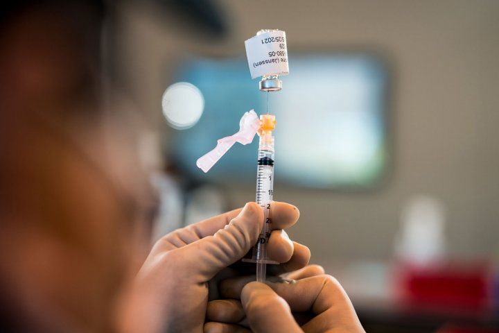 Gloved hands drawing vaccine from vial into syringe