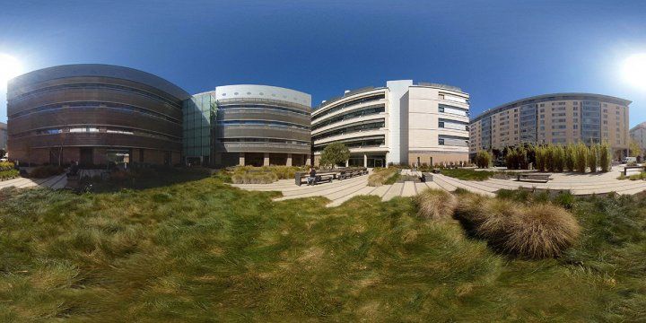 A grassy courtyard sits behind two UCSF buildings with a series of benches and tables that allow people space to rest and relax