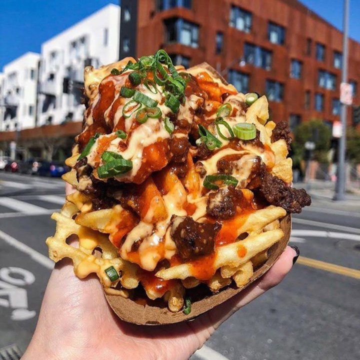 A hand holding up a massive pile of french fries covered in barbecue sauce and other condiments