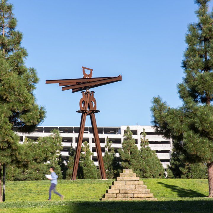 A person walks across the Quad with an impressively large Dreamcatcher in the background