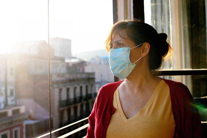 Woman wearing mask, looking out window