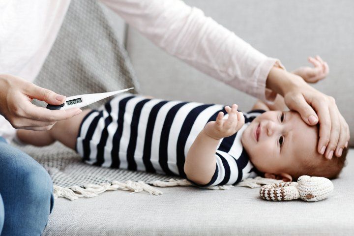 a woman holds a thermometer with one hand while holding her other hand to a newborn's forehead