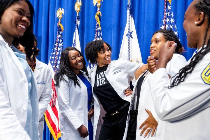 UCSF obstetrician and gynecologist Dr. Andrea Jackson speaks with colleagues, all in white coats. A blue curtain and American flags are in the background