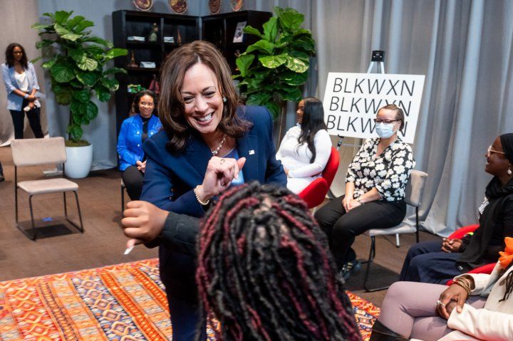 Vice President Kamala Harris elbow greets an attendee at an event for Black mothers in San Francisco. In the background is a white sign with black letters reading "BLKWXN"