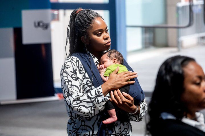 UCSF clinical psychologist Theresia Oklan, PhD, holds her one-month-old son Maayan. A Black woman is standing in front of her, watching VP Harris speaking.