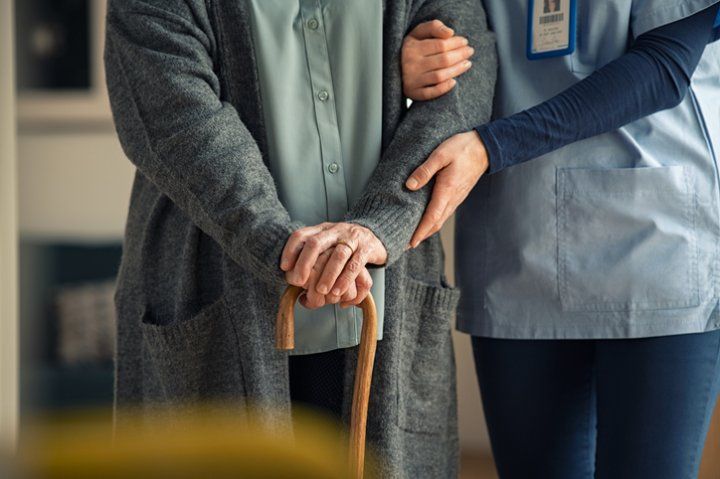 Nurse holds arm of elderly woman with a cane