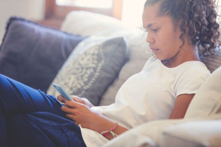 A pre-teen girl looking upset with mobile phone. She is sitting on the sofa at home.