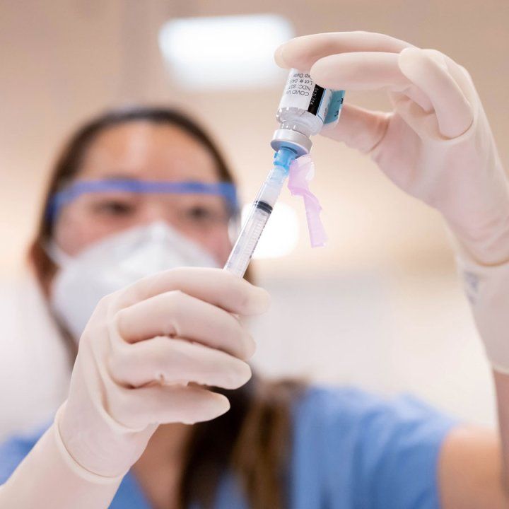 Regina Lai, pharmacy technician at UCSF, examines a dose of the Moderna COVID-19 vaccine