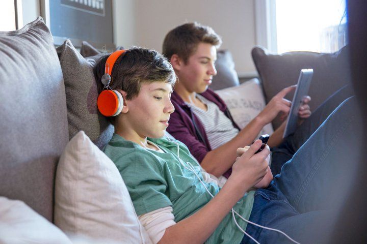 Two white teen boys with a digital tablet and smart phone sit on a sofa at home