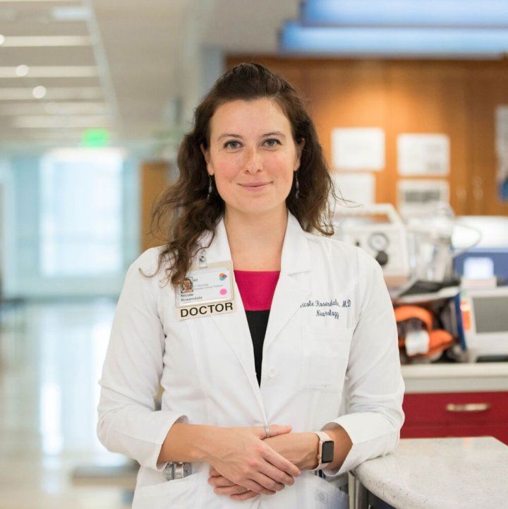 Nicole Rosendale, MD, stands in a hospital lobby wearing a doctor's lab coat