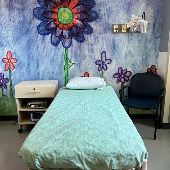 A child-sized cot sits in front of a mural with blue flowers.