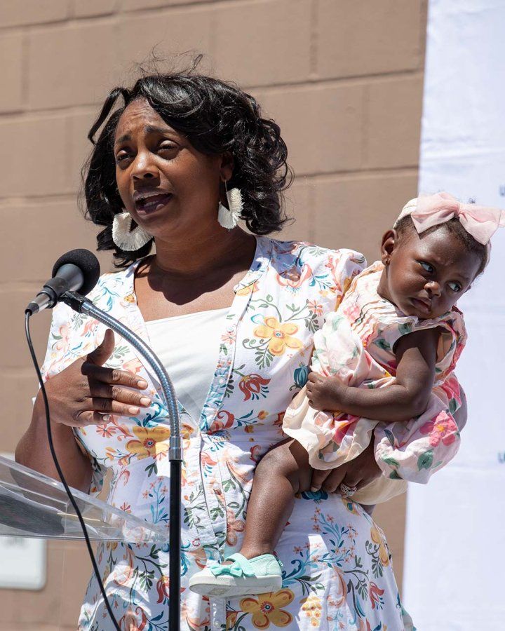 A mom speaks at a podium holding her baby daughter during the launch of the clinic.
