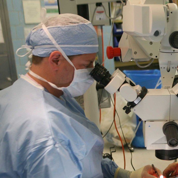 Surgeon Scott Hansen looks into a microscope as he performs microsurgery on an arm.