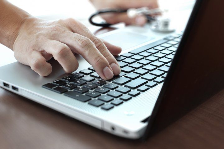 Hands holding a stethoscope and using a laptop.