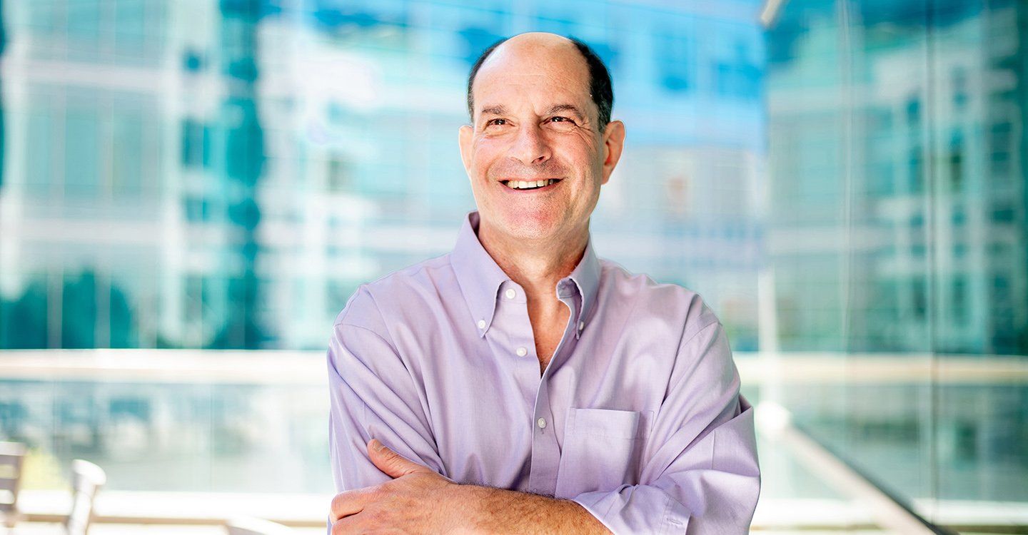 David Julius smiles and stands proudly against a bank of windows on the Mission Bay campus