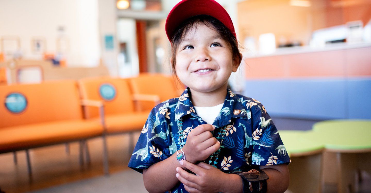 A small boy wearing a baseball cap smiles upward at the Benioff Children's Hospital in San Francisco