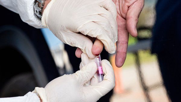 Gloved hands performing finger prick blood test
