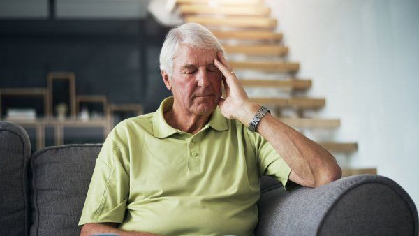 Elderly man sitting on couch with hand touching head